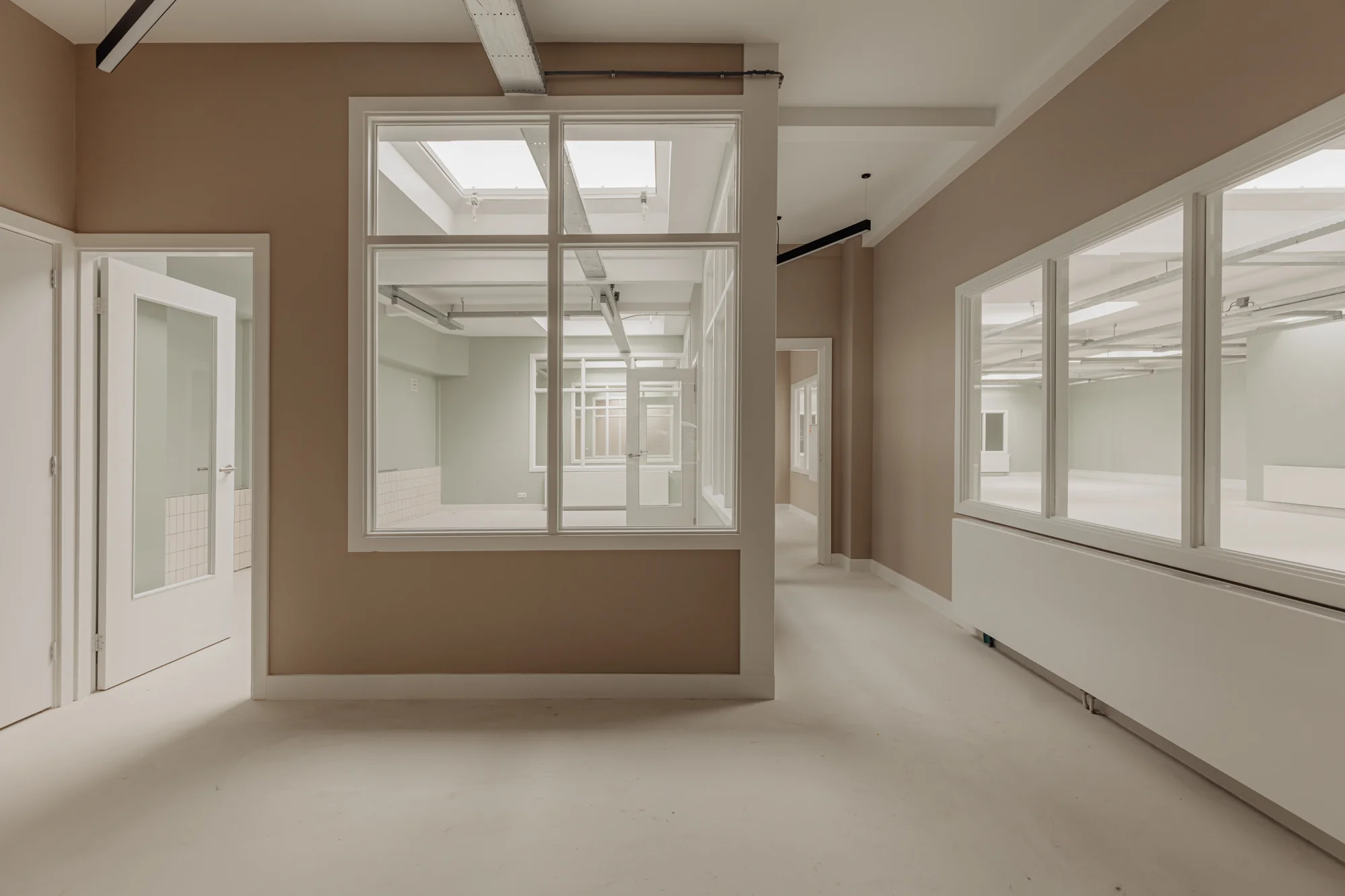 Licht en modern interieur van een gerenoveerd kantoorpand aan de Henri Polaklaan met glazen binnenwanden en beige muren.